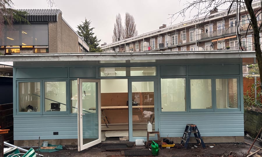 Tuinpaviljoen in aanbouw met lichtblauwe houten gevel en grote glaspuien, in een Amsterdamse achtertuin